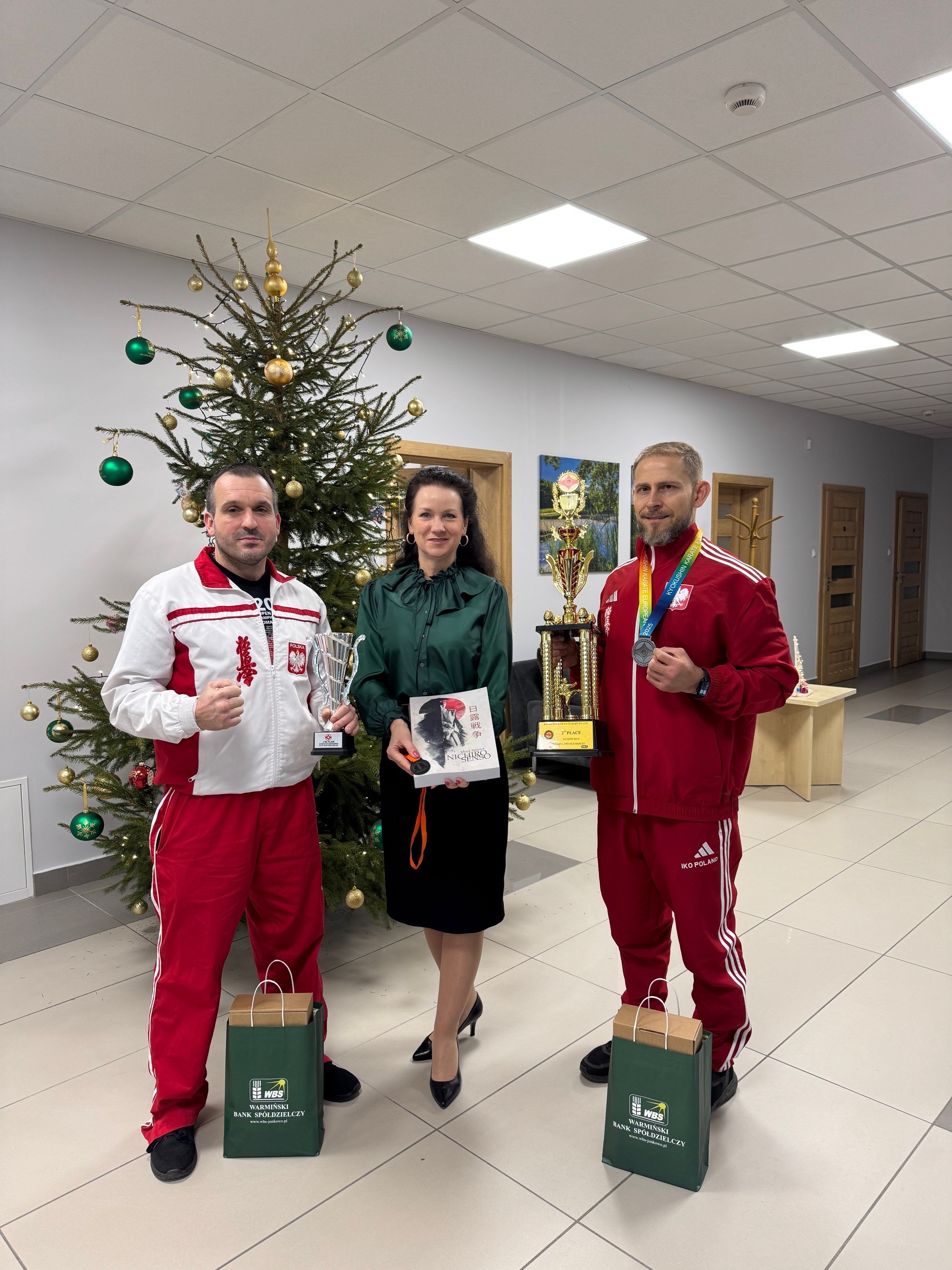 Zdjęcie zawodników z pucharami oraz Pani Prezes Katarzyny Siemaszko na tle choinki w centrali banku